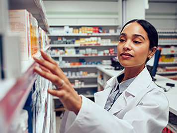 Young woman working in pharmacy looking for medicine standing behind counter