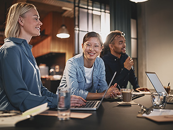 Smiling Asian businesswoman leaning on a table in an office during a meeting with a diverse group of colleagues