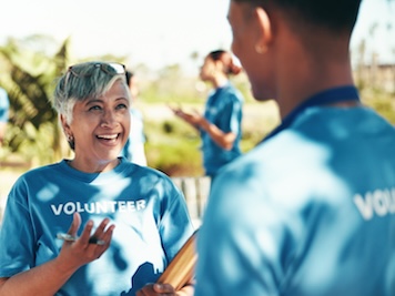 Teamwork, volunteers and happy for charity, group and success of fundraiser, discussion and mature woman. Outdoor, talking and coordinator with good news for people, community service and nonprofit.